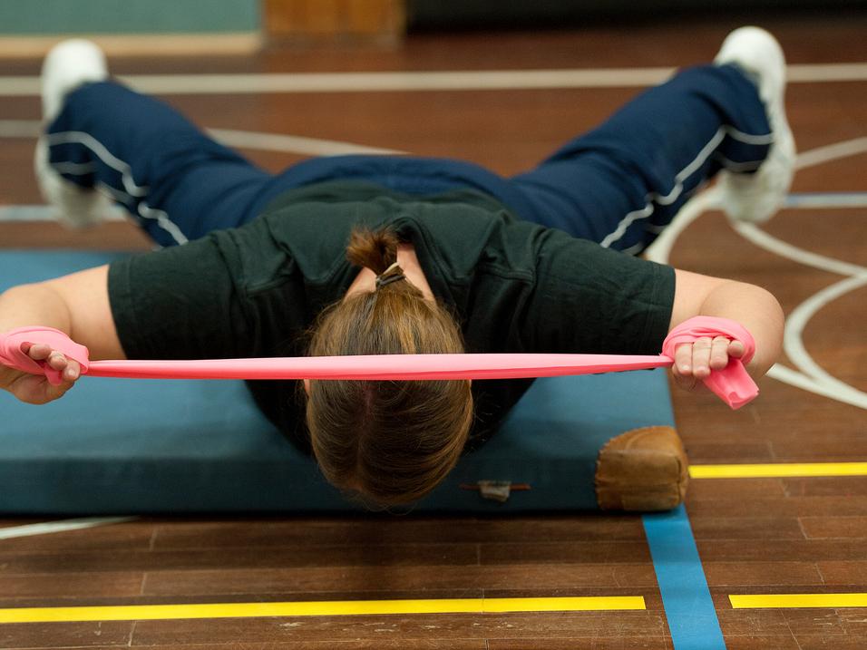 Frau führt eine Übung mit einem pinken Widerstandsband auf einer Matte in einem Sportbereich aus.